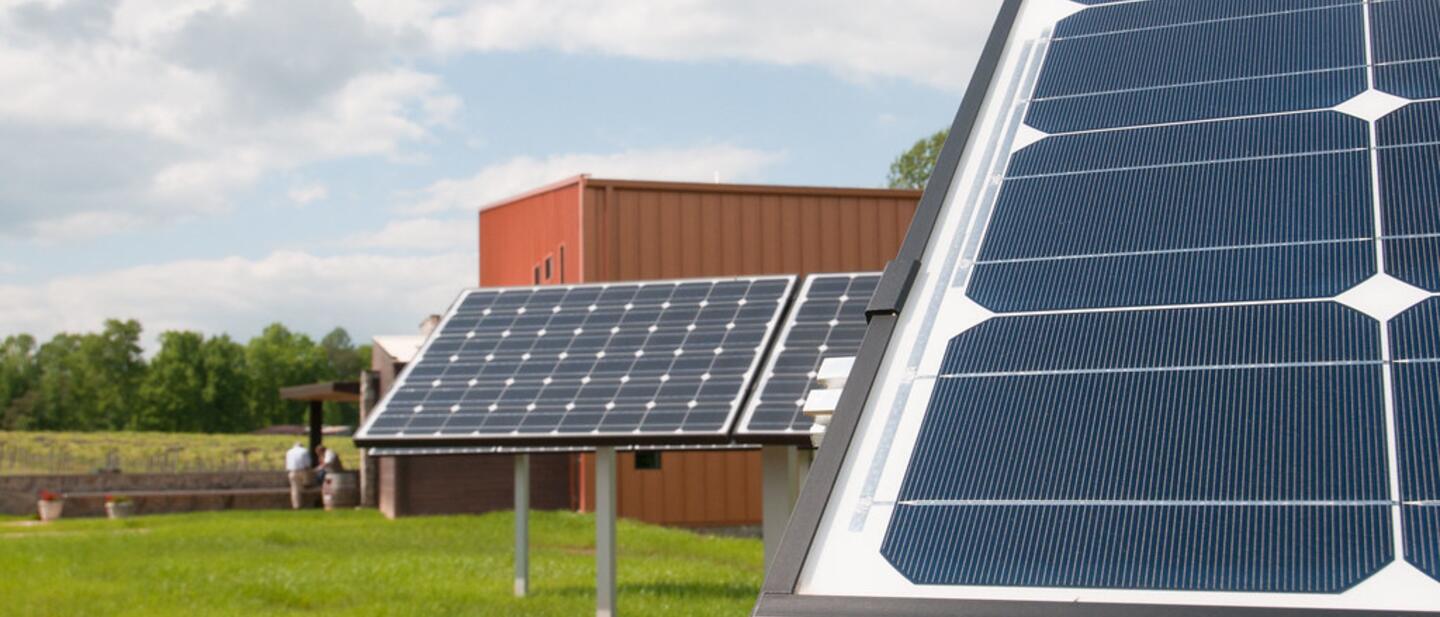 A ground-mounted solar panel array on open grassland under a bright sky